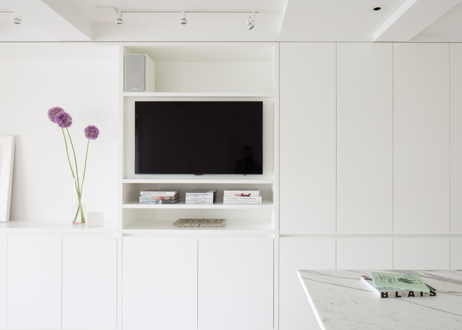 TV nook with white cabinets and purple flowers by Wettling Architects