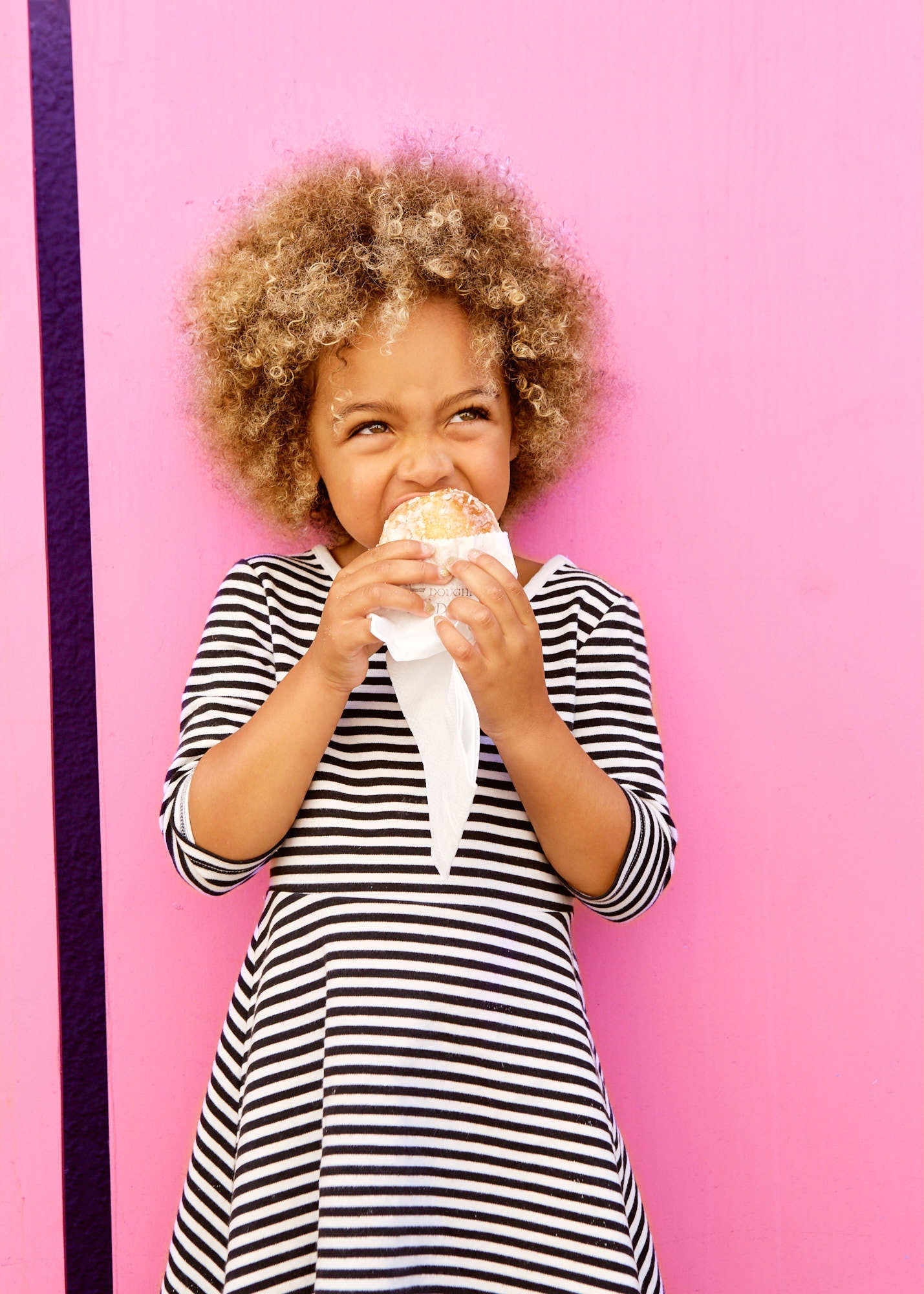 Cute little girl eats pastry against bright pink wall in Temescal Alley
