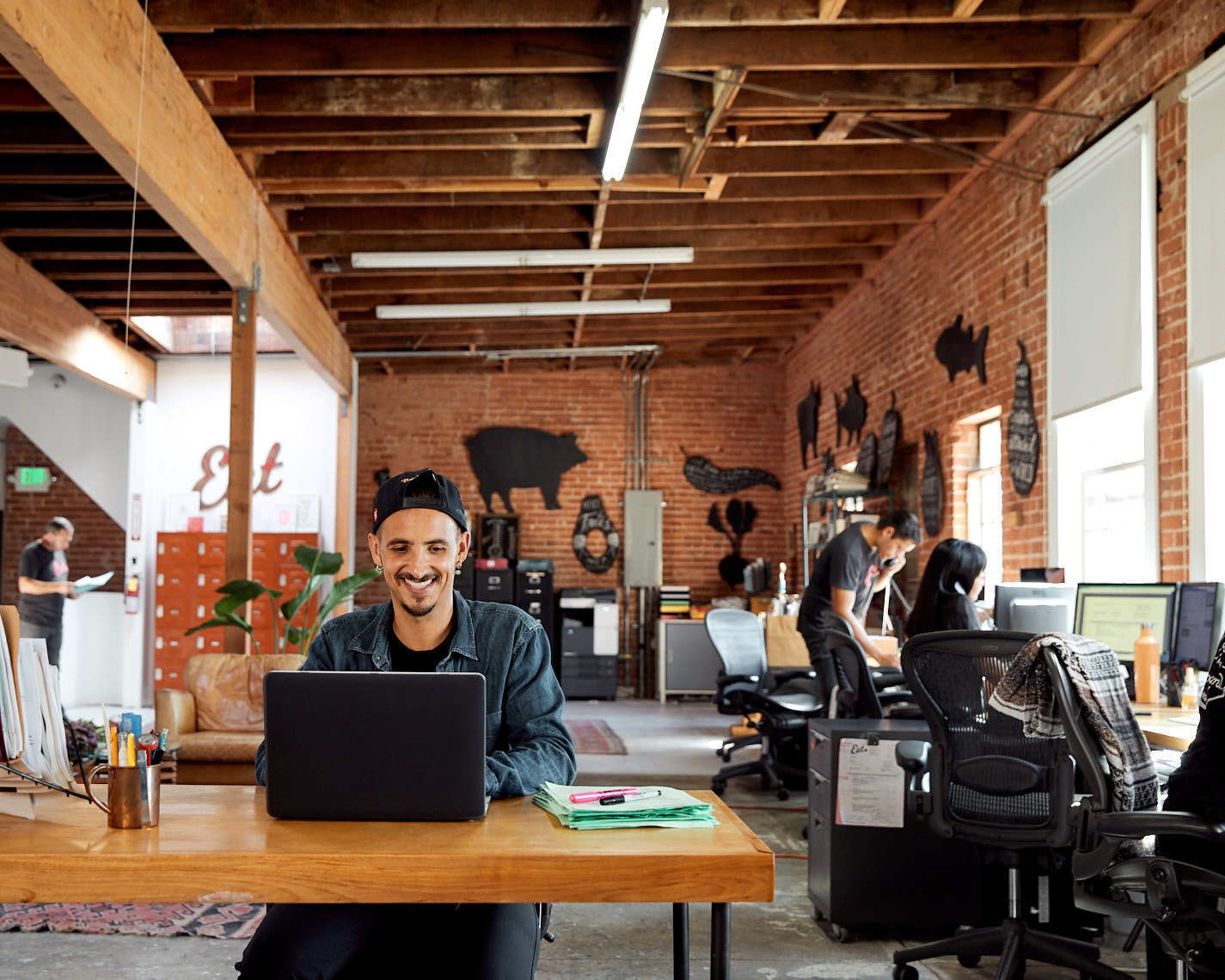 Young man sits in brick office space with coworkers on their laptops