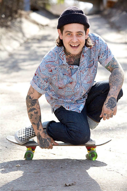 Tattooed male model Justin Kitchen rides skateboard with beanie and colorful shirt