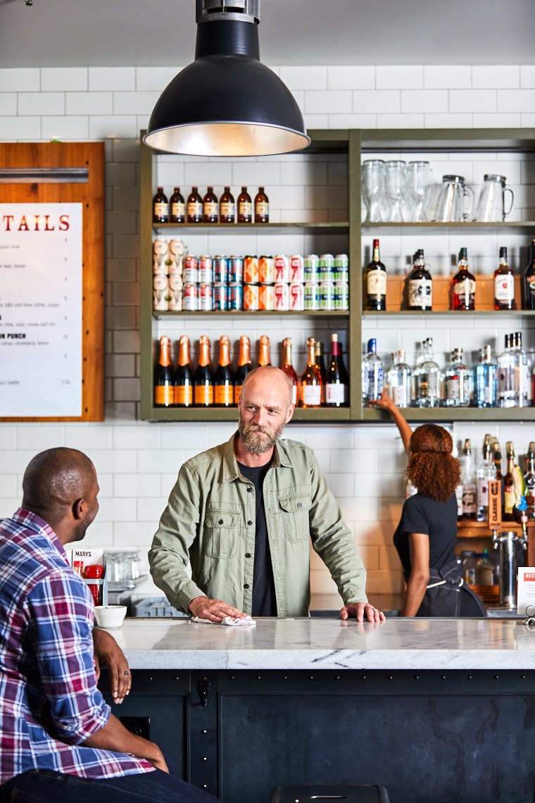 Male bartender stands behind bar helping customer at West Egg