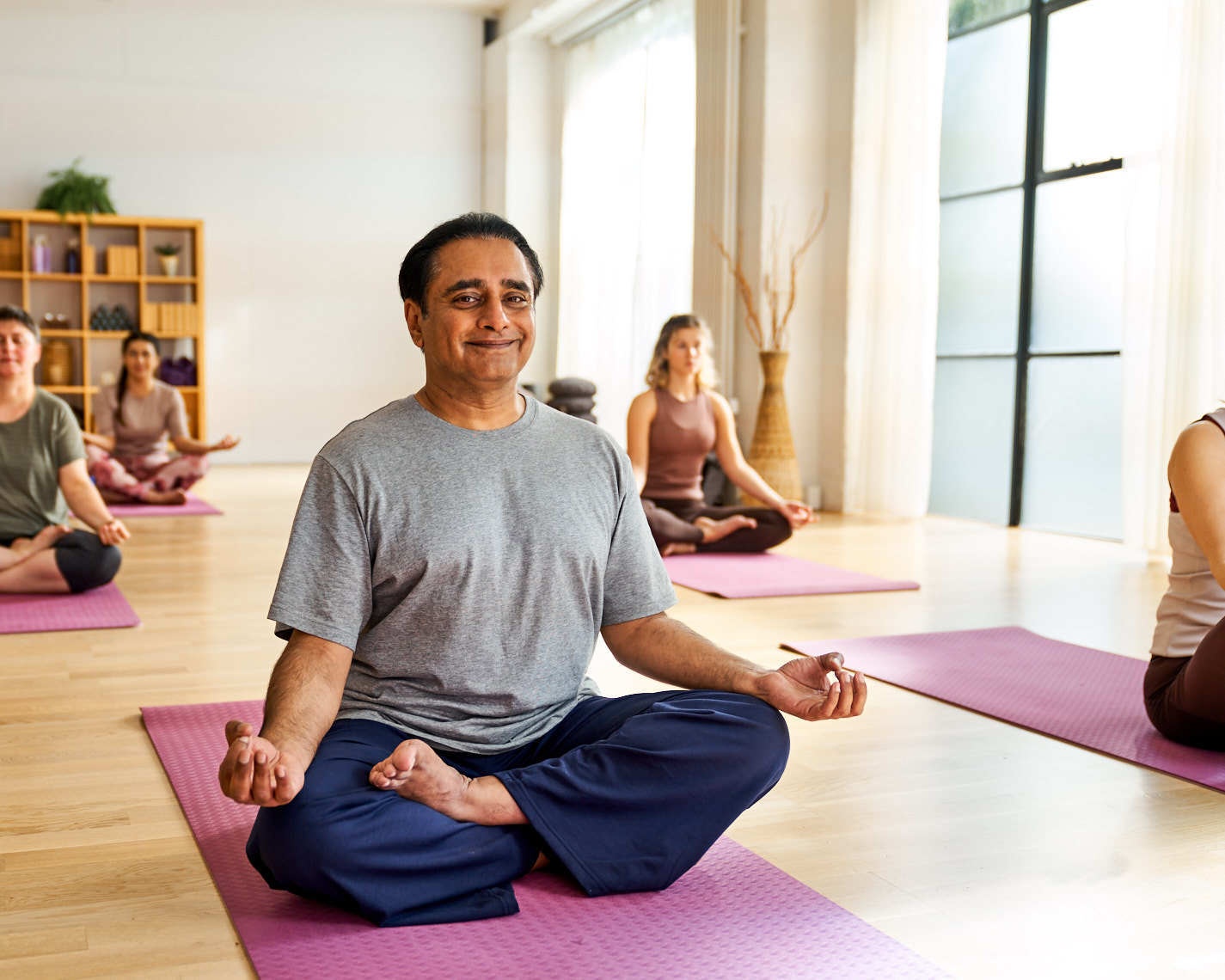 Man sitting in half lotus on purple yoga mat in studio