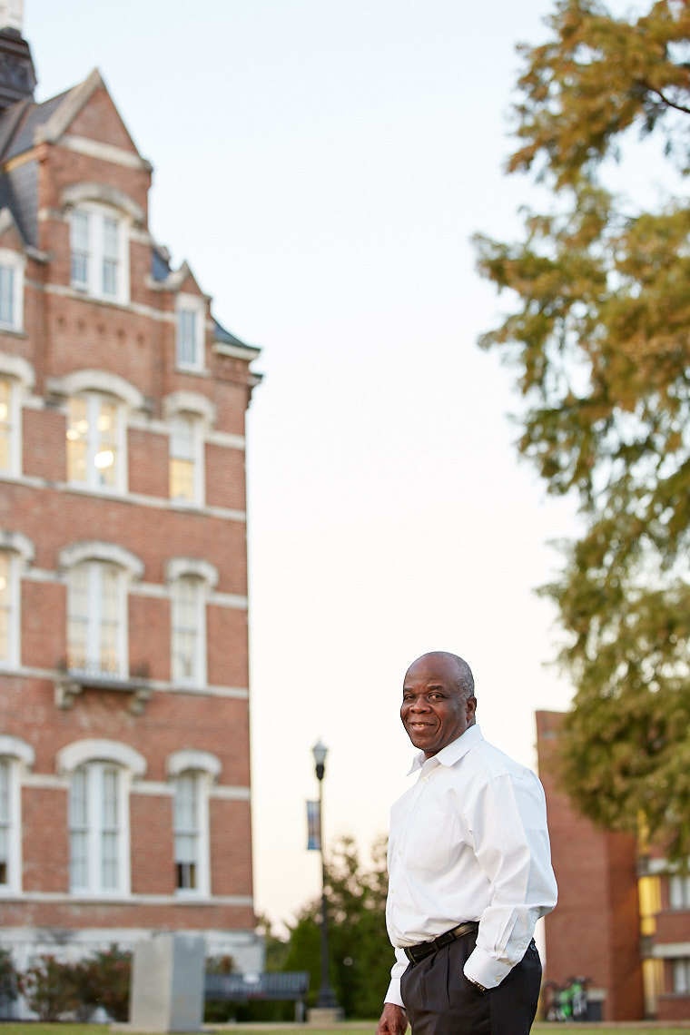 Man in white button down and black pants in front of college campus