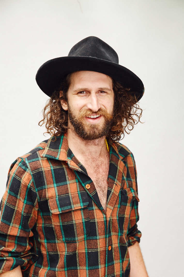 White man with curly hair wearing a black hat and plaid button down shirt