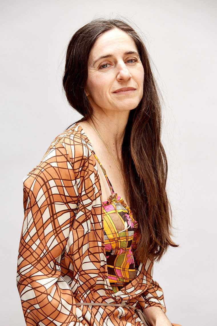 Woman with long brown hair wearing orange 70s style blouse