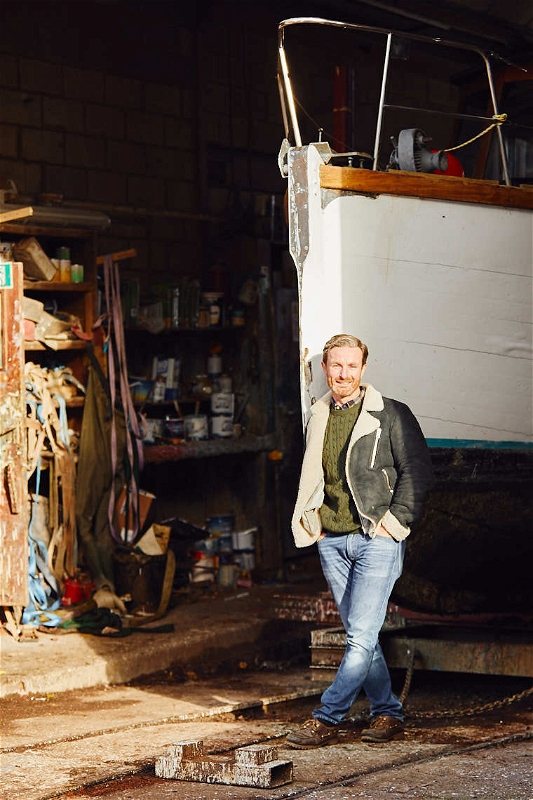 Michael Dennett boat builder man stands in front of wooden boat