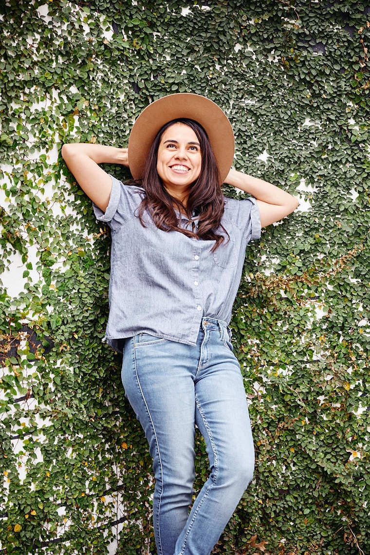 Woman Ale Gonzalez posing in sun hat against green vine wall
