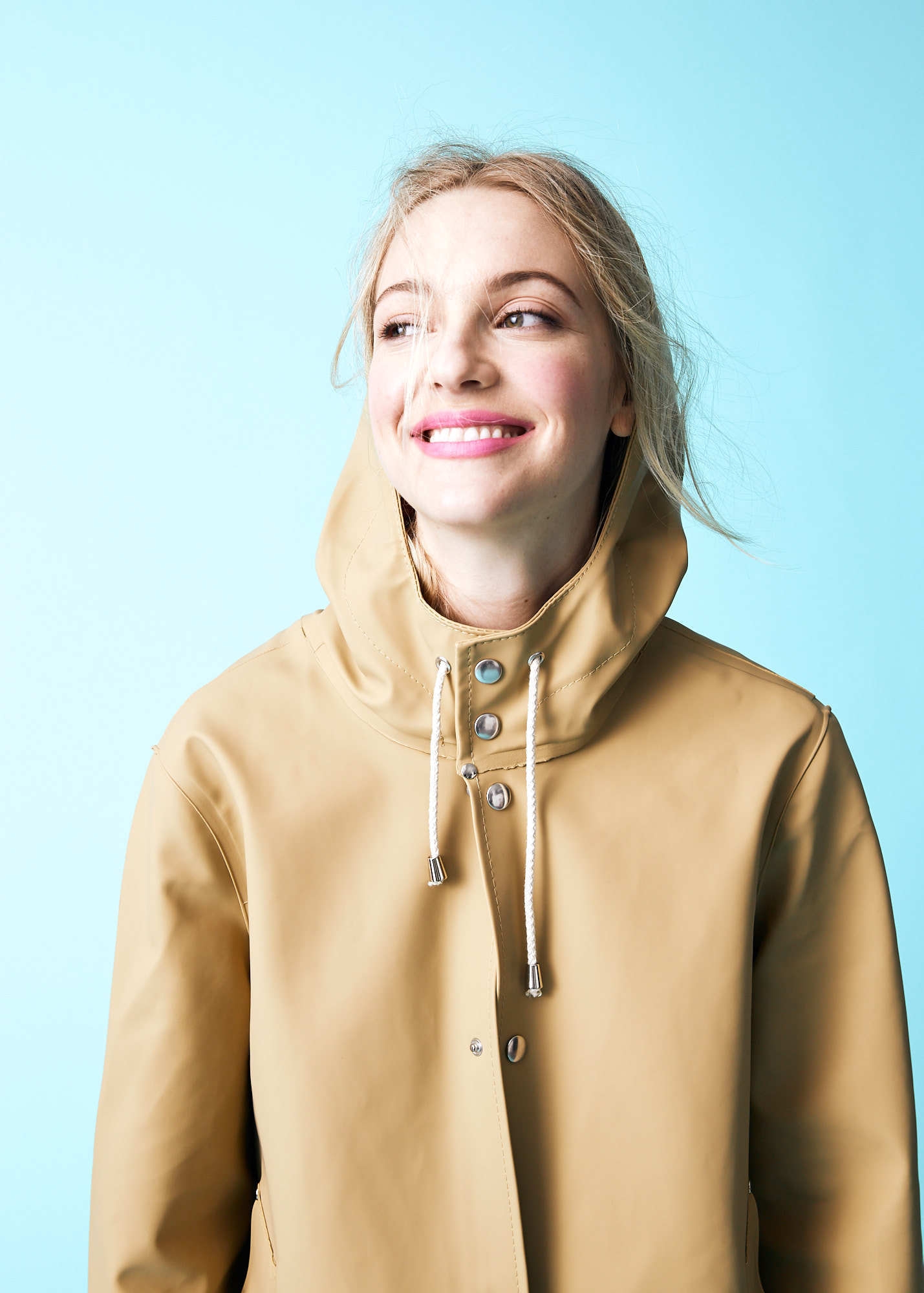 Editorial portrait of blonde woman in tan raincoat and pink lipstick